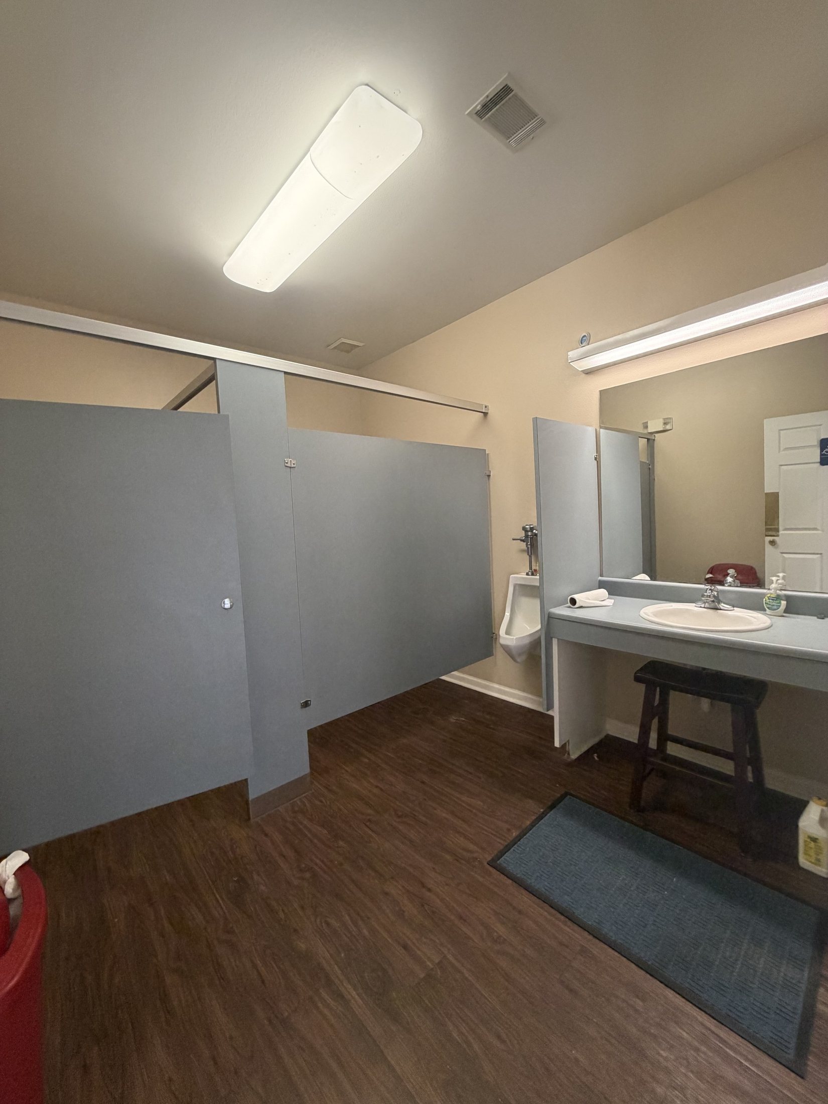 Before: the men’s restroom with grey partitions and fluorescent light